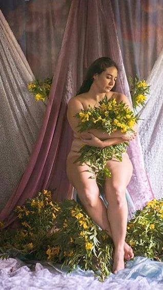 Alejandra Porta sentada entre telas, abrazando flores amarillas
