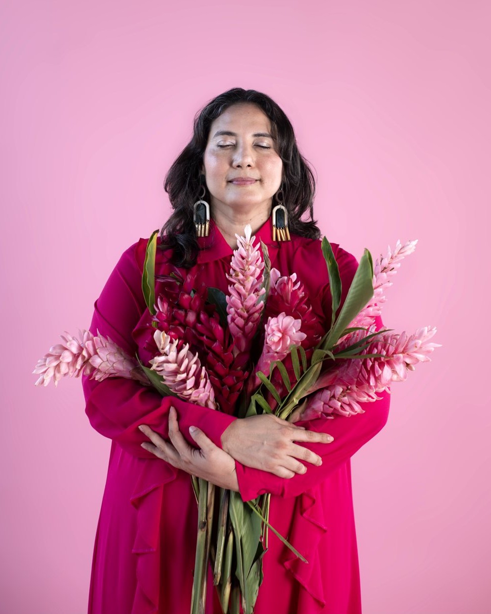 Alejandra Porta con los ojos cerrados, abrazando un ramo de flores de jengibre rosa
