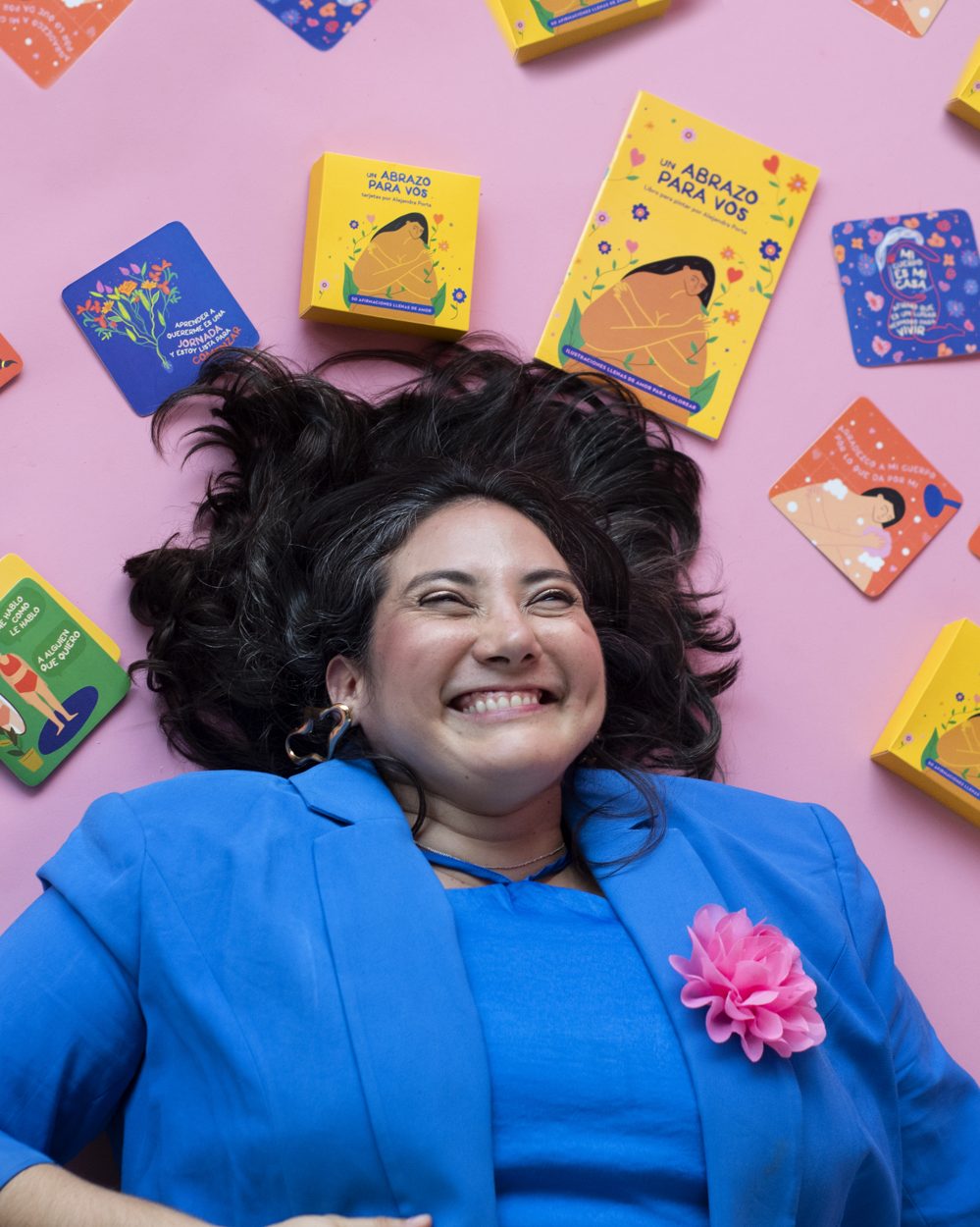 Ale riéndose en un piso rosa rodeada de sus cartas de afirmación y su libro para pintar