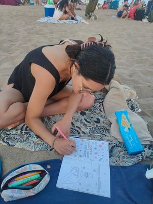 Una mujer pintando el libro de Ale sobre una toalla en la playa