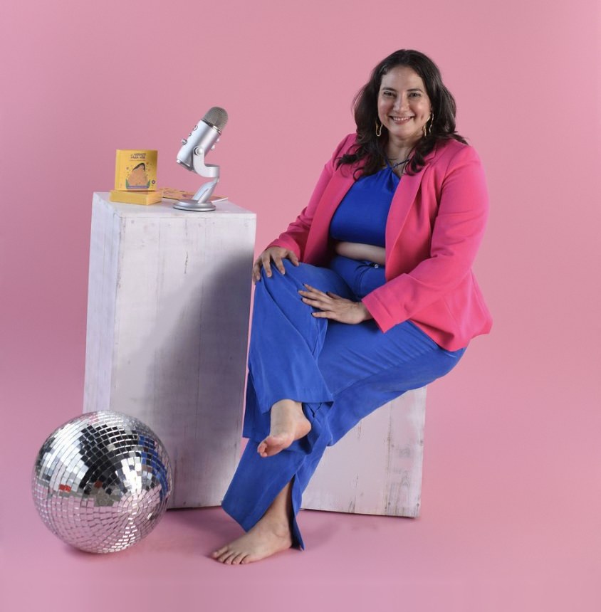 Ale sonriendo, sentada junto a un micrófono de podcast y sus cartas de afirmación